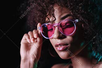 Alluring unusual girl with curly afro hair corrects her glasses. Sexy woman with perfect makeup looking at camera and