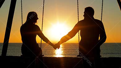 Couple swinging holding hands at sunrise