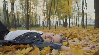 Happy boy lays on yellow leaves in autumn park