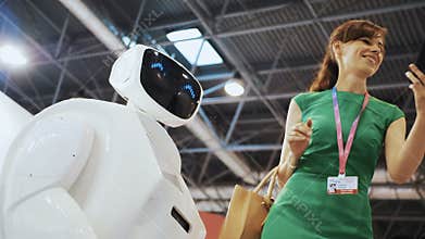A beautiful girl does selfie with a robot. Robot flirts with the woman. Modern Robotic Technologies. The robot looks at