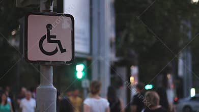 Sign of a disabled person sitting on a wheelchair against the background of blurred walking people. Concept idea