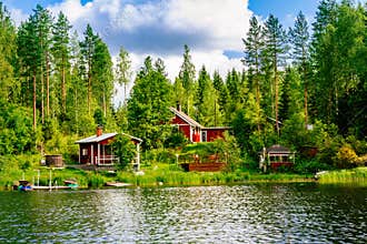 A traditional Finnish wooden cottage with a sauna and a barn on the lake shore. Summer rural Finland.