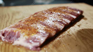 Professional spinkles seasoning on pieces of meat on table in kitchen.