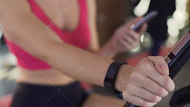 Fitness bracelet on womans hand, athletic girl riding exercise bike, closeup