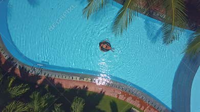 Woman lies on back on ring sailing along pool