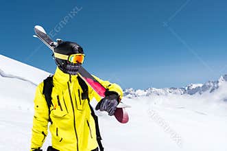 Skier standing on a slope. Man in a light suit, the helmet and mask in skiing is to ski. In the background snow-capped