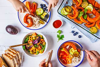 Family eating a healthy vegetarian food. Vegan lunch table top view, plant based diet. Baked vegetables, fresh salad, berries,