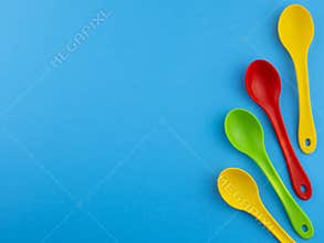 Yellow red and green plastic spoons on blue background with copy space for text