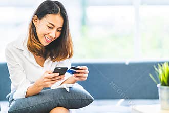 Young beautiful Asian woman using smartphone and credit card for online shopping at home with copy space. E-payment technology