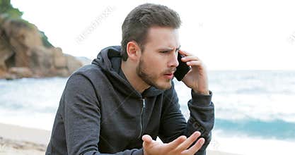 Angry man calling on phone on the beach