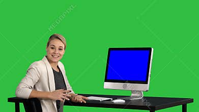 Confident focused businesswoman talking to camera and looking to monitor near her on a Green Screen, Chroma Key. Blue