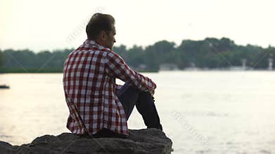 Depressed adult male sitting on riverside and thinking about divorce, loneliness