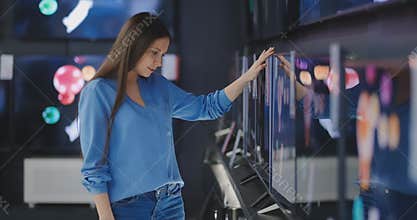 Smart modern female customer choosing large TV-sets at electronics store. New screen generations.