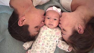 Smiling family in bed, where the cool face plan is dad, mom and little daughter, parents gently kiss their baby.