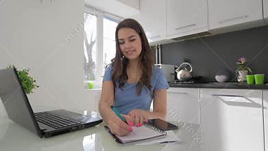Freelance work, happy young woman working on laptop computer while cooking in kitchen
