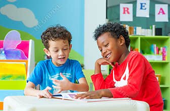 Two boy kid sit on table and reading tale book in preschool lib