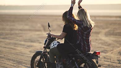 Beautiful young woman motorcyclist with his girlfriend riding a motorcycle in a desert on sunset or sunrise. Girlfriends on a bike
