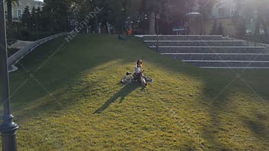 Woman cyclist lying on green grass in park and using mobile phone