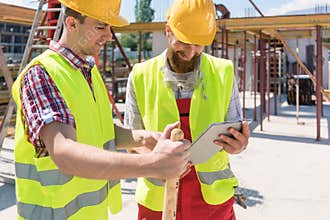 Two young construction workers smiling while using a tablet duri