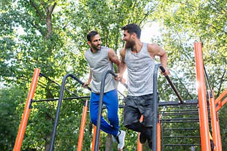 Two handsome young men passionate about fitness doing dips exerc