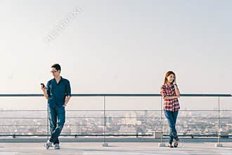 Asian couple using telephone call and smartphone together on building roof. Mobile cellphone device or information technology