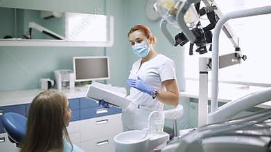 A woman stomotologist talking to a girl with a patient in a dental office