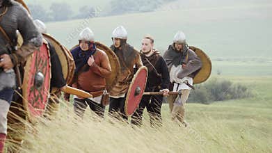 Group of Viking with shields walking forward on the meadow