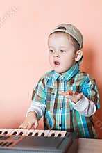 Cute boy wearing baseball cap backwards playing the digital piano
