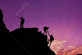 Hikers climbing on rock, mountain at sunset, one of them giving hand and helping to climb.Teamwork , Helps ,Success, winner and Le