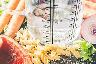 500 ml - ccm Water In A Measuring Cup Surrounded By Noodles, Pepper, Onion, Carrots And Spices