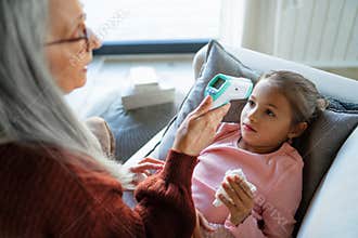 Grandmother taking care of her ill grandchild lying on sofa