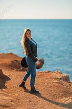 A blonde in a stylish black leather jacket walks along the seashore.