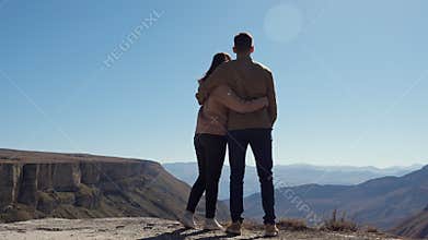 Young couple in love over the cliff admire the view of the valley on a clear sunny day