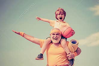 Sportsman grandfather and healthy kid with basketball ball on blue sky background. Sport for little children. Different