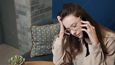 Portrait of a tired woman talking on the phone at home. Caucasian sad woman freelancer speaks on a smartphone on a sofa