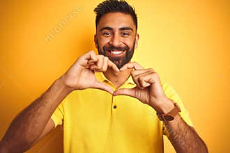 Young indian man wearing polo standing over isolated yellow background smiling in love showing heart symbol and shape with hands