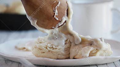 Woman`s hand using a spoon to pour hot gravy over buttermilk biscuits.
