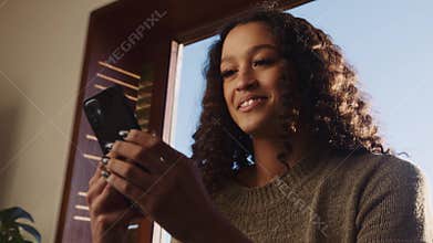 Young, happy, African-American female relaxing at home texting on cellular device whilst watching television