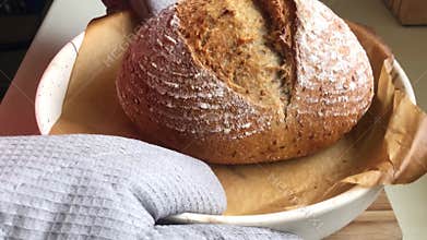 Baker puts freshly baked sourdough bread on wooden board.