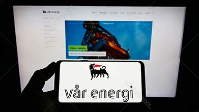 Person holding cellphone with logo of oil and gas company Var Energi on screen in front of webpage.