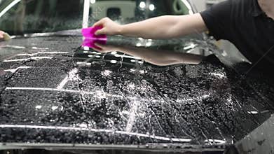 Smoothing the protective film on the car. The worker-detailer smoothes the protective film with the help of a working