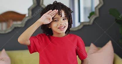 Portrait of happy biracial boy looking at camera and saluting