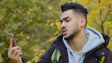 Young man standing outdoors lagged behind tourist group lost in wood traveling with backpack answering mobile call no