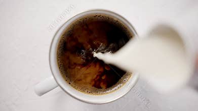Adding cream to a cup with black, hot coffee placed on white table