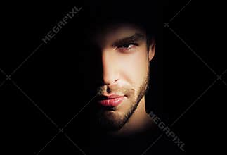 Closeup portrait of handsome man with strong look standing in dark light in studio on black background