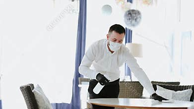 Waiter cleaning white table at the restaurant by disinfection bottle.