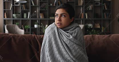 Indian woman sit on sofa feeling cold covered with plaid