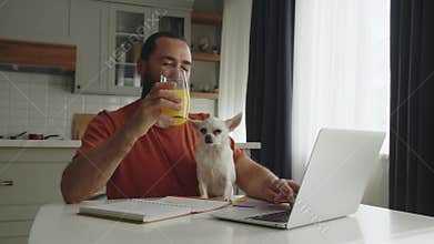 A young bearded man sits at the kitchen table together with a pet friend, a white dog of breed chihuahua, strokes it and