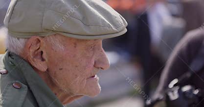 A close-up view captures an elderly man engaged in conversation, enjoying a cigar, and sporting a vintage hat, exuding a