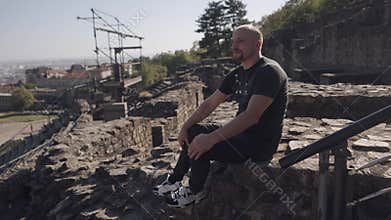 Man sitting peacefully on ancient ruins, enjoying the panoramic view of the cityscape